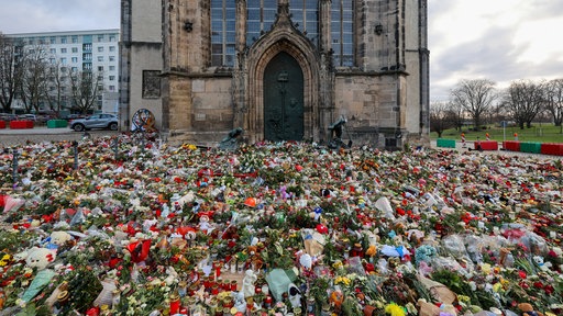 Das Bild zeigt den Magdeburger Dom mit hunderten Blumen, Kerzen und Kuscheltieren davor.