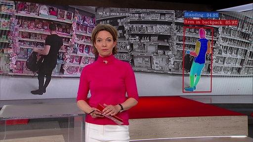 Anna Planken steht im Markt-Studio im Hintergrund sieht man Sicherheitskameraaufnahmen aus verschiednene Läden.