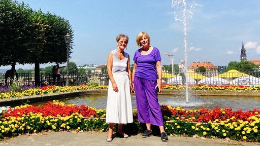 Zwei ältere Frauen stehen vor einem Teich, der umringt ist von roten, weißen und gelben Blumen.