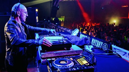 Ein DJ steht auf der Bühne vor den Feiernden bei der Mayday in Dortmund und dreht an den Reglern seines Turntables.