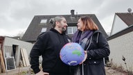 Kassra und Nelli Taheri stehen vor ihrem Haus und halten eine aufgeblasene Weltkugel fest