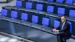 Weite Aufnahme von Friedrich Merz allein im Bundestag sitzend