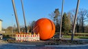Zu sehen ist eine orangene Stahlkugel in einem Stahlgerüst.
