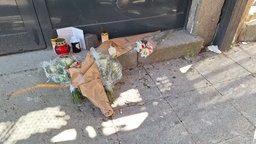 Blumen und Kerzen liegen auf dem Boden vor dem Textilfachgeschäft in Krefeld. 
