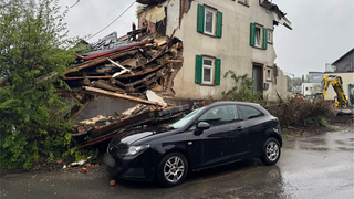 Ein Auto parkt neben einem Haus, dessen Außenwand auf das Auto gestürzt ist
