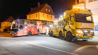 Ein Mannschaftsbus steckt auf einer steilen Straße fest, ein Bergungsfahrzeug steht daneben.