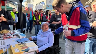 Ein Demonstrant schaut einen Menschen im Rollstuhl an, beide lächeln