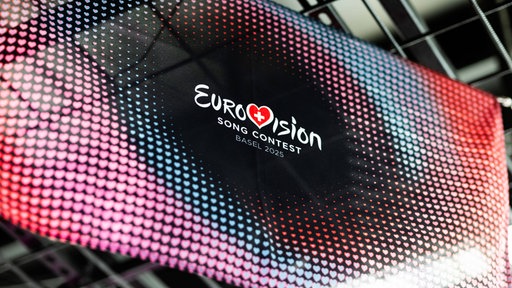 Fahne auf schwarz-rotem Hintergrund, mit der Aufschrift Eurovison Contest 2025 unter Dachkonstruktion